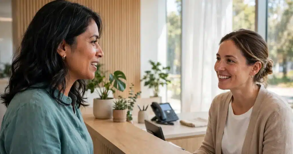 Photo of a woman in her 40s checking in at the bright reception desk of a modern imaging centre before her mammogram