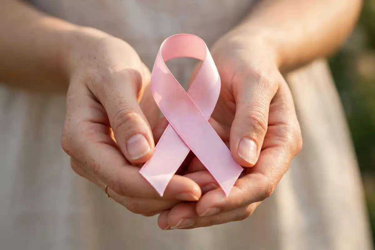 Photo of a woman's hands holding a plain pink satin awareness ribbon against a soft neutral background